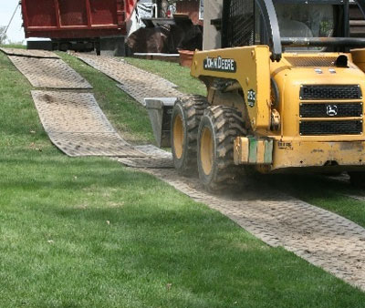 Front loader driving on ground protection mats laid over grass